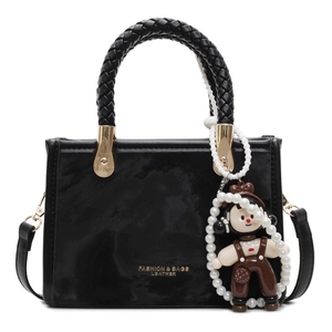 Minimalist black faux leather handbag with woven handle, pearl chain, and doll charm accessory