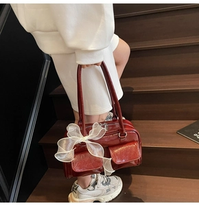 Detail of wine red glossy Boston bag with large white mesh bow and front pockets