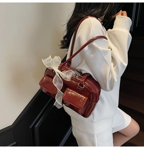 Close-up of deep red glossy leather shoulder bag with white mesh bow and buckle pockets