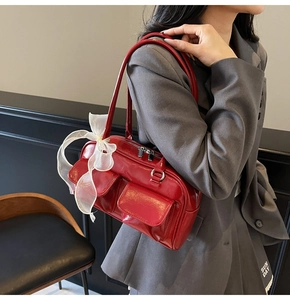Detail of red glossy shoulder bag with dual front pockets and white lace bow accents