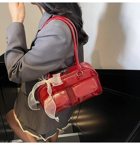 Detail view of red glossy shoulder bag with twin front pockets and lace bow accessory