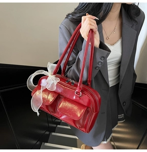 Detail of red glossy shoulder bag with utilitarian pockets and a white lace bow accent