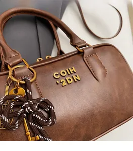 Close-up of textured brown leather handbag with gold logo and woven keychain detail