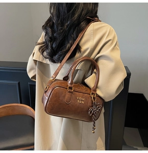Detail showing deep brown vintage faux leather Boston bag with knot charm and gold logo