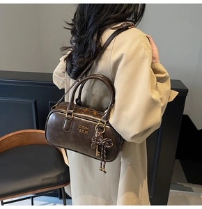 Detailed side view of a vintage dark brown Boston bag with gold hardware and charm