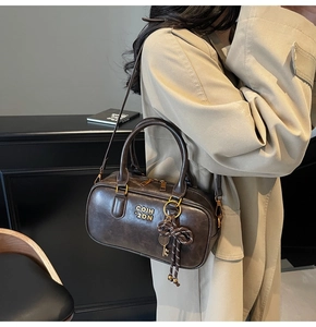Detail of dark brown leather Boston bag featuring metal logo and vintage charm pendant