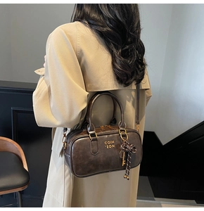 Detail of vintage brown leather handbag featuring metal pendants on a khaki trench coat