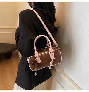 Detail of two-tone crossbody bag with pink handle and decorative key pendant on model