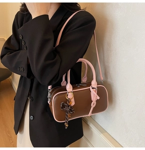 Close-up of contrast stitching, pink handles, and a bow charm on a retro brown Boston bag