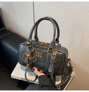 Detail of dark gray washed leather boston bag with gold lettering and decorative key charm