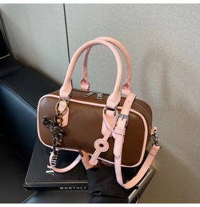 Detail of Boston bag with pink trim, key charm, and adjustable strap on a dark base