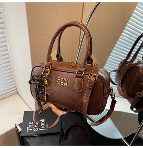 Detail of retro dark brown leather boston bag with metal logo and woven charm