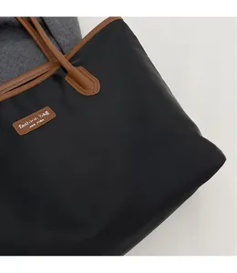 Detailaufnahme des schwarzen Nylongewebes und braunen Leder-Logos auf der Shopper-Tasche