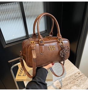 Detail view of brown vintage cylinder bag with gold metal logo and braided pendant