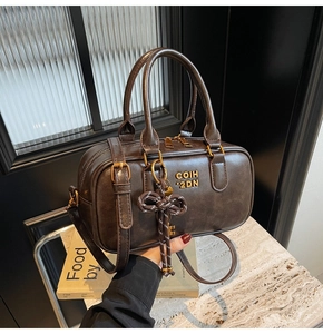 Detail shot of a dark brown vintage Boston bag featuring a woven bow charm and gold logo