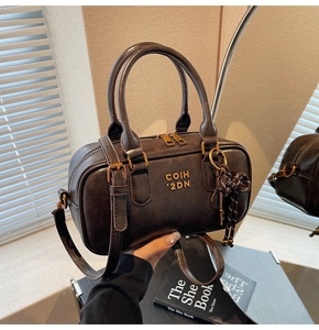 Detail of dark brown leather Boston bag with gold logo, bow charm and textured hardware