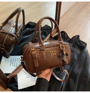 Detailed close-up of brown leather Boston bag with gold logo and tennis racket charm