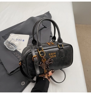 Detail of black textured leather bag with gold hardware and butterfly keychain charm