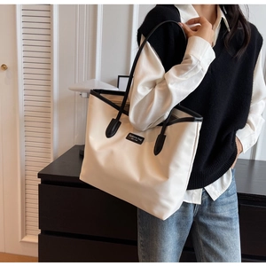 Detail einer großen beigen Oxford-Tasche mit schwarzem Lederbesatz und modischem Label