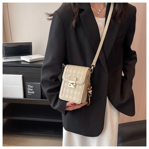 Detail of a beige quilted crossbody bag with gold buckle and cute bear pendant accessory