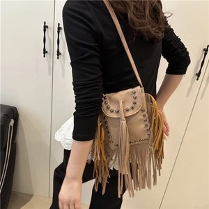 Khaki leather crossbody bag with long tassels and rivet details worn by a model