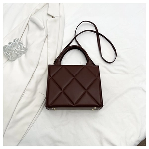 Detail view of coffee brown quilted handbag featuring large diamond pattern and base studs