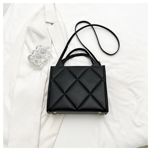 Close-up of black quilted handbag with golden bottom studs and detachable strap