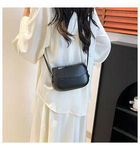 Minimalist black saddle crossbody bag shown on a model in a modern interior setting