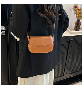 Gros plan du sac besace marron caramel porté avec un blazer noir et jupe blanche