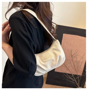 Dettaglio di una borsa a tracolla intrecciata color crema con pieghe e logo patch