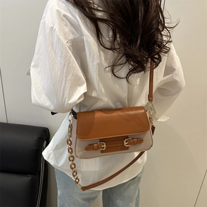 Bolso bandolera retro bicolor con solapa marrón y hebilla metálica mostrado con un modelo