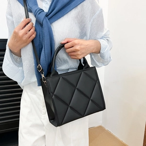 Chic black quilted tote bag with top handle and adjustable strap in minimalist setting