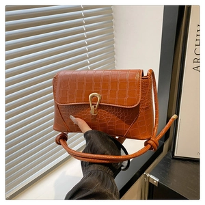 Detail of caramel crocodile pattern handbag featuring a gold horseshoe buckle and leather strap