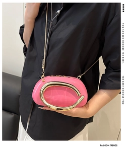 Close-up of bright pink hard shell clutch with large gold C-shaped metal handle and chain