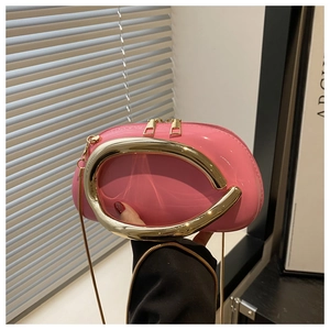 Detail of pink lacquer crossbody bag featuring a large U-shaped golden metal handle