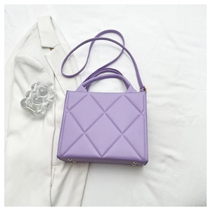 Detailed view of purple quilted handbag with gold studs on bottom over white fabric
