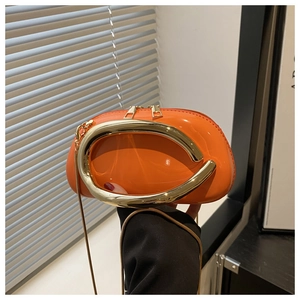 Detail of orange glossy mini bag with large gold C-handle and fine metal chain strap
