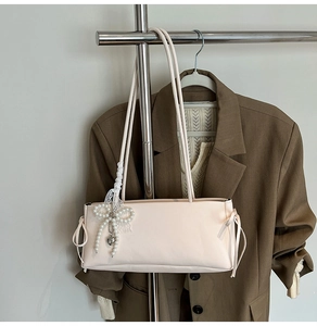 Detail of light pink shoulder bag featuring a lace pearl bow and silver heart pendant