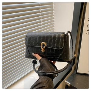 Detail of black crocodile texture handbag with gold metal lock and leather strap