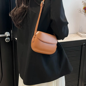 Minimalist brown leather saddle bag for women with adjustable strap worn by model