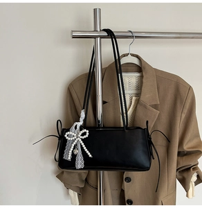 Detail der schwarzen matten Ledertasche mit weißer Perlen-Spitzenschleife und Herzanhänger