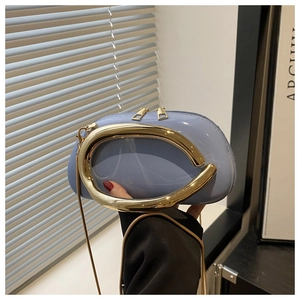 Detail of light blue patent leather bag featuring bold gold curved metal handle and chain
