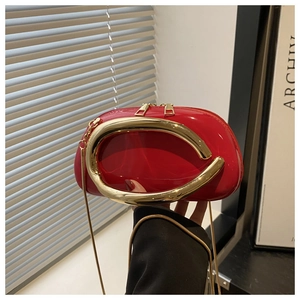 Detail of red acrylic shell bag with metallic C-handle and gold snake chain strap