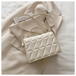 Detail of cream quilted crossbody bag with gold hardware on a beige blazer background