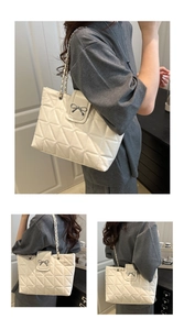 Detail of white quilted tote bag featuring a silver bow clasp and metal chain straps