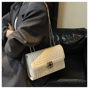 Detail of a quilted beige chain crossbody bag with black gemstone buckle on a model