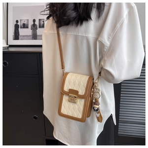 Detail of a quilted crossbody phone bag with brown trim and cute cow charm on a model