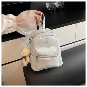 Detalle de una mini mochila blanca de cuero PU con colgante de oso y logotipo central