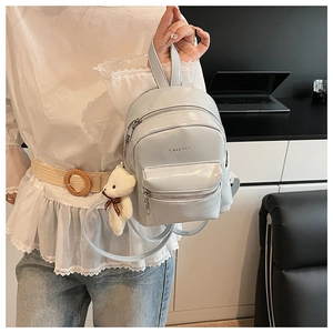 Primer plano de la mini mochila de charol azul claro con colgante de oso y cremalleras