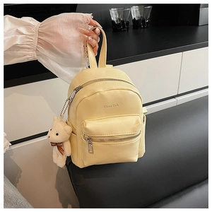 Detalle de una mini mochila amarilla con un oso de peluche blanco y cremalleras metálicas
